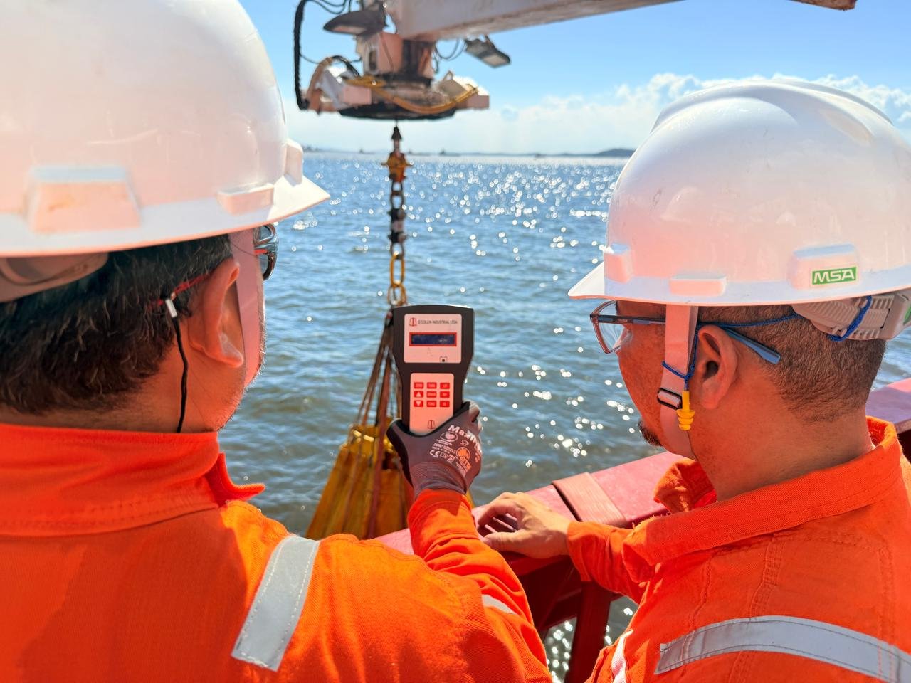 Dois técnicos com dinamômetro certificado durante teste de carga de guindaste offshore